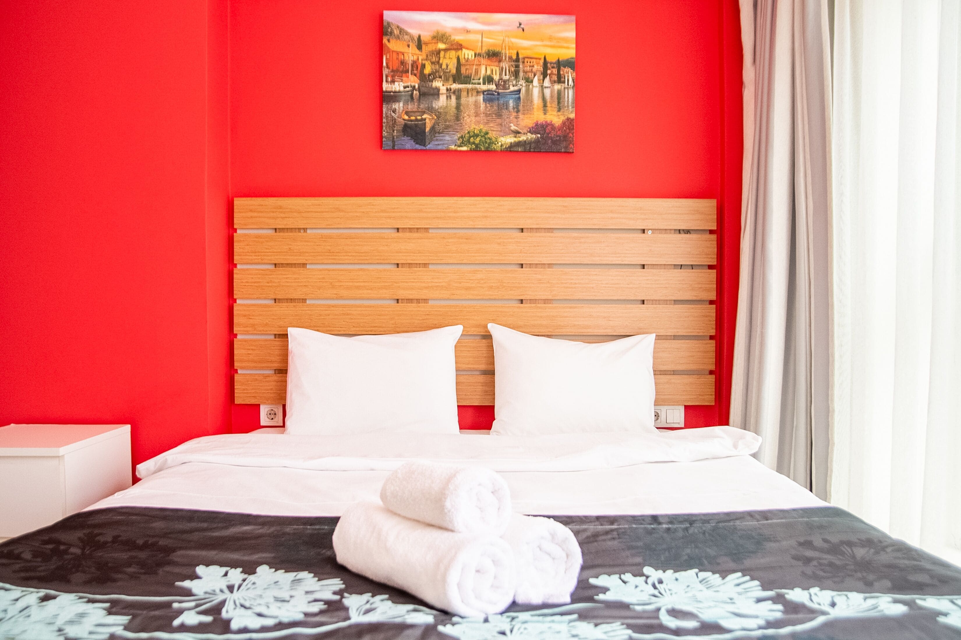A hotel room with a wooden headboard, white bedding, and a painting of a cityscape on the wall.