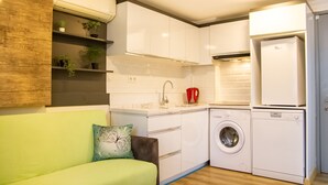 A compact kitchen with white cabinets, a washing machine, and a built-in oven. - Fi Homes - Adults Only (Izmir)