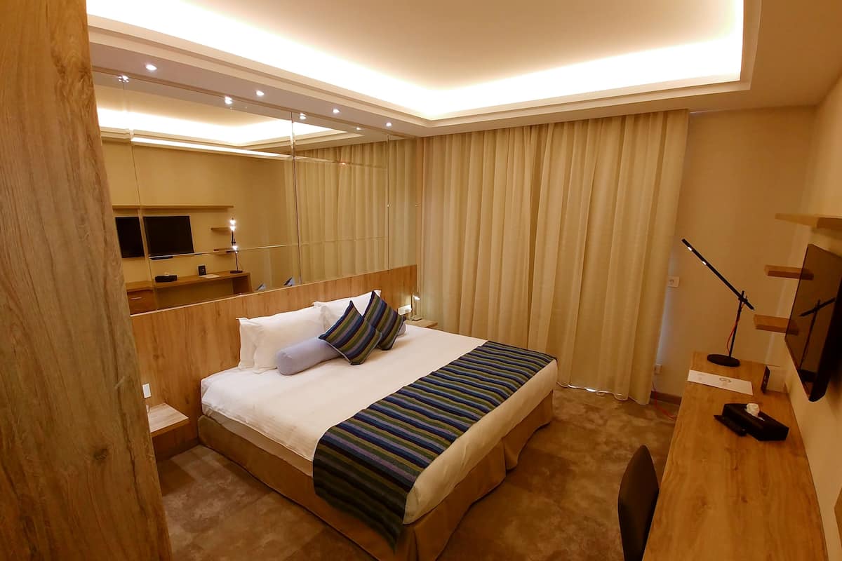 A modern hotel room with a large bed, wooden headboard, and a flat-screen TV mounted on the wall.
