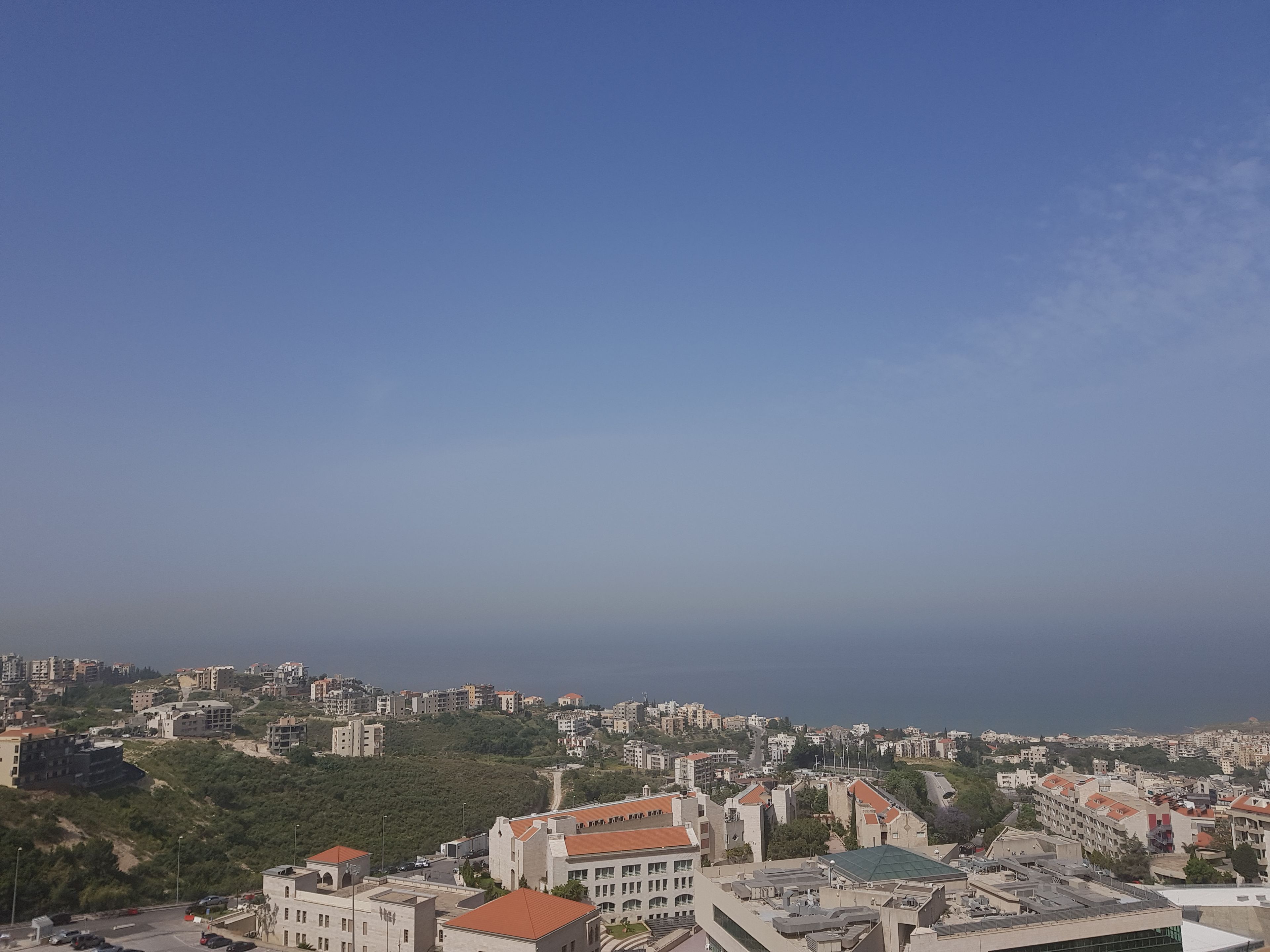 A cityscape with a mix of residential and commercial buildings, a clear sky, and a hilly terrain in the background.