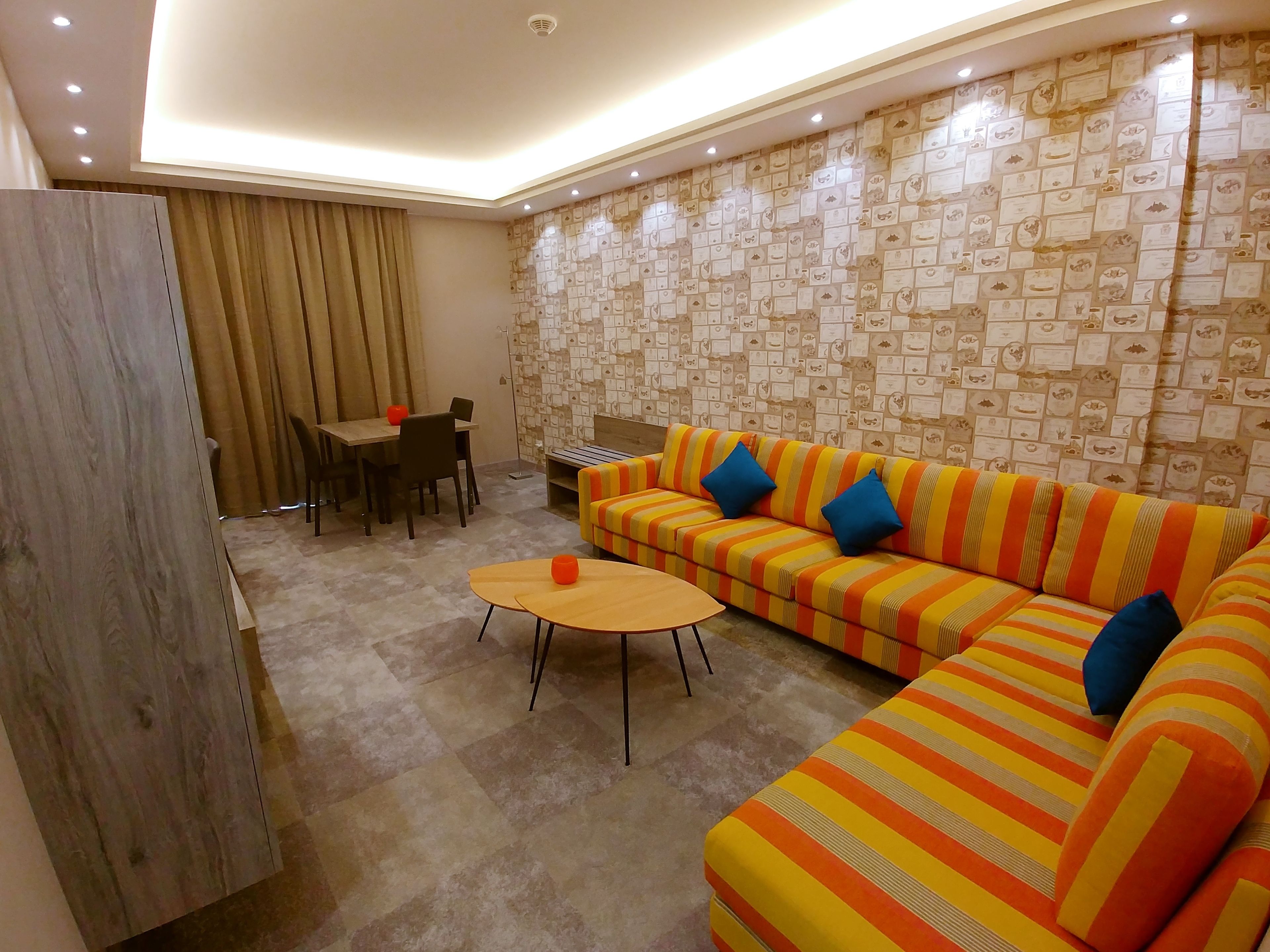 A modern living room with a striped sofa, a dining table, and a wall decorated with certificates.