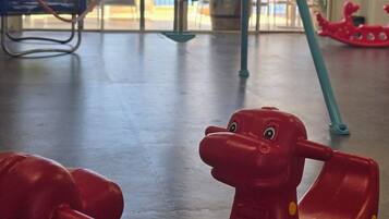Zona de juegos infantiles con columpios y un caballo de juguete rojo.