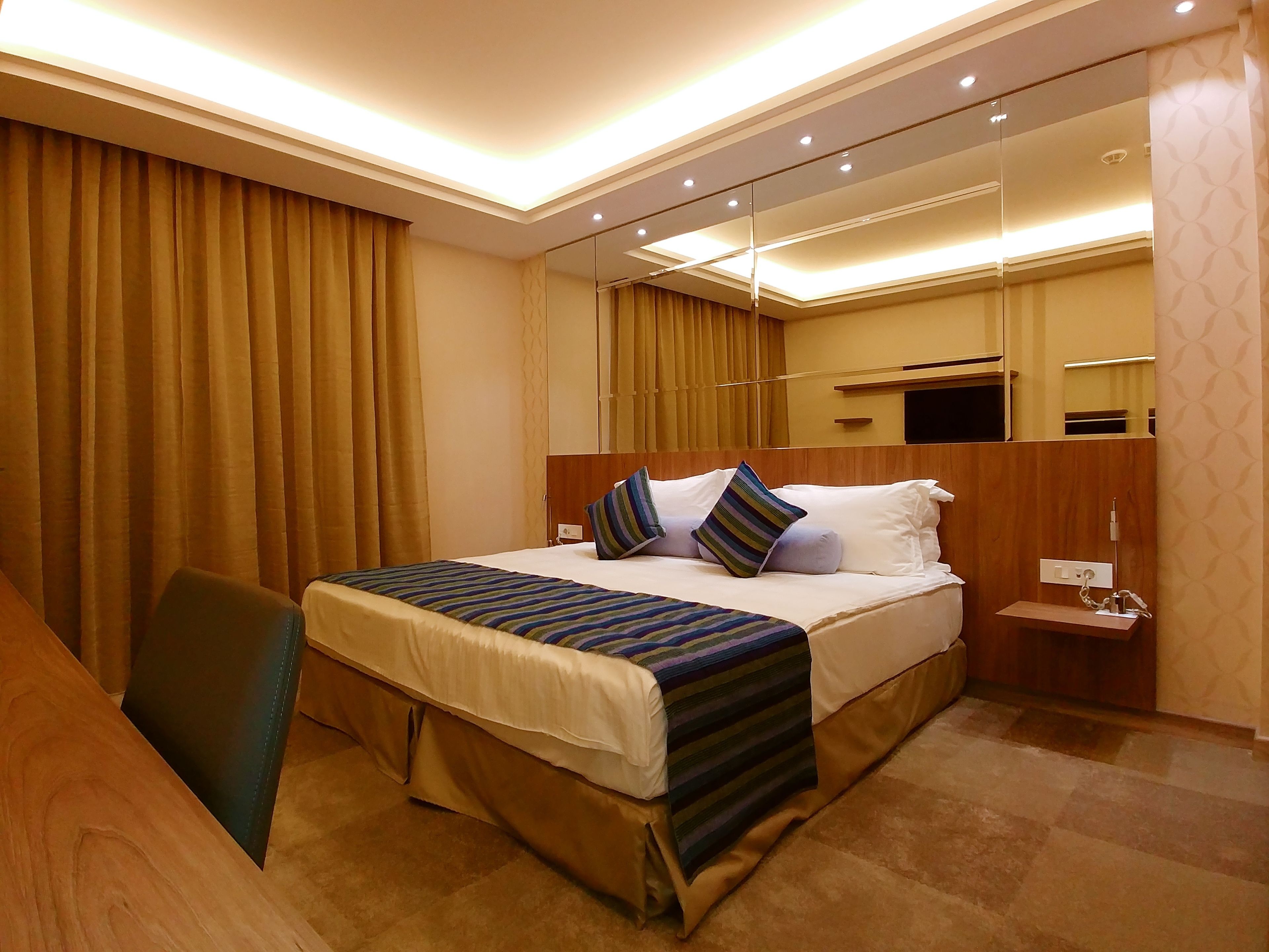 Quarto de hotel com uma cama grande, mesa de cabeceira, espelho e escrivaninha.