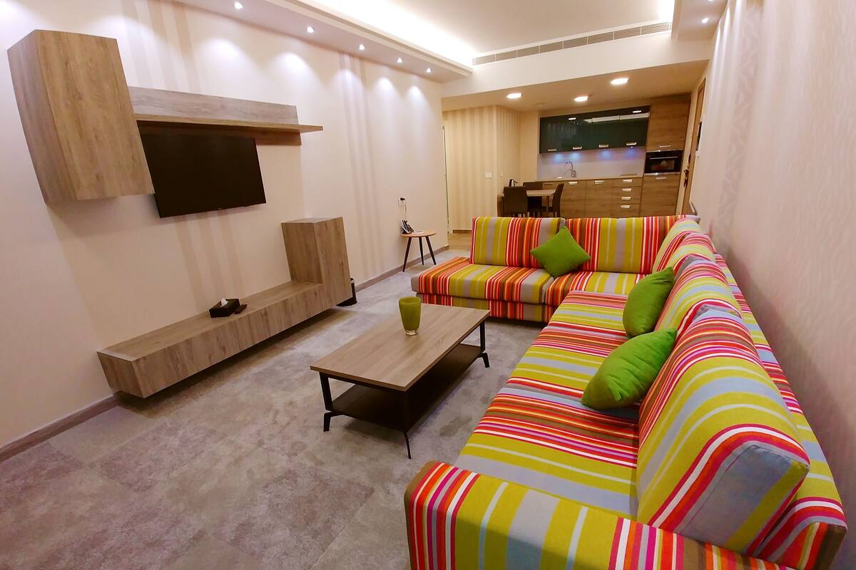 A modern living room with a sofa set, a coffee table, and a TV mounted on the wall.