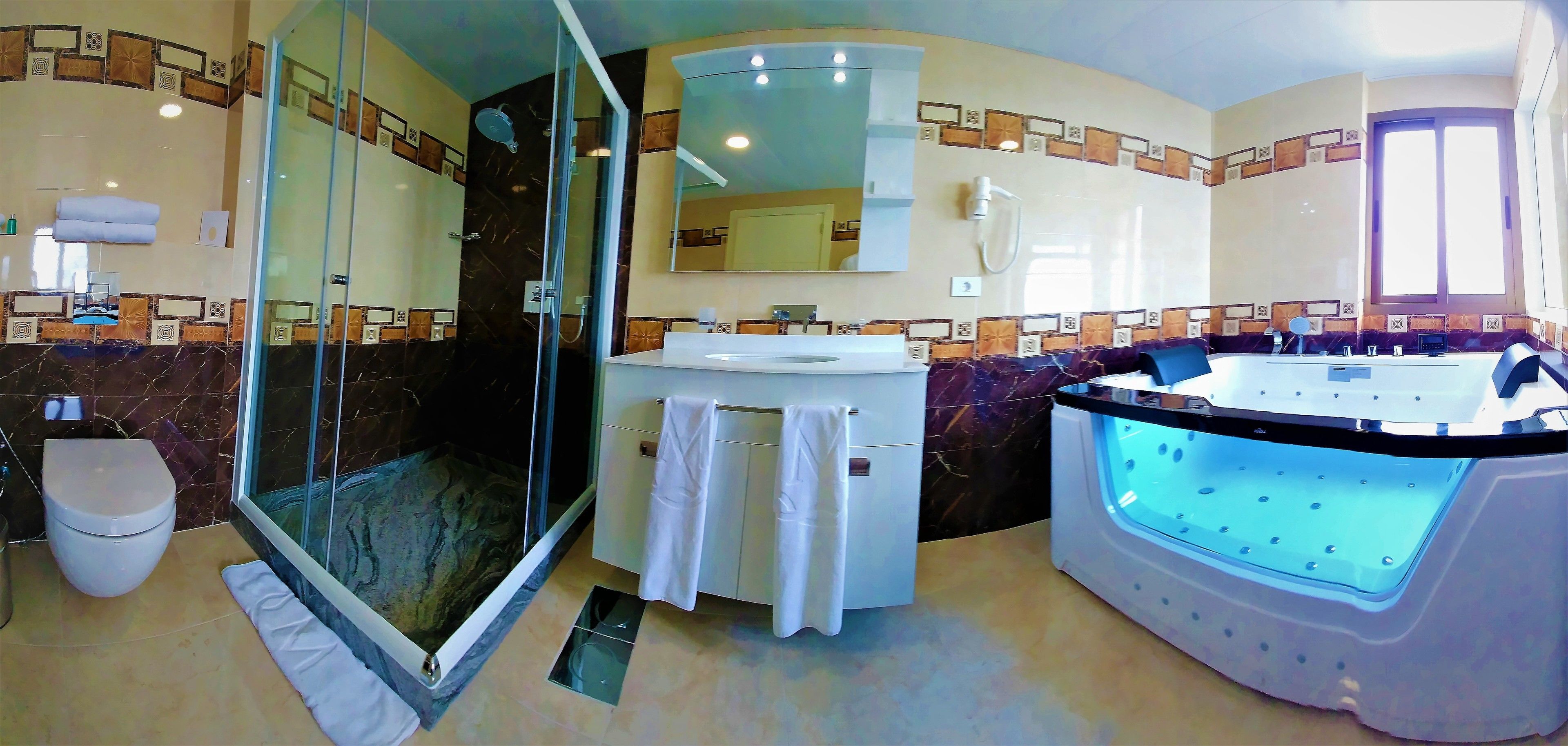 A bathroom with a glass-enclosed shower, a sink with a mirror, and a heated bathtub.