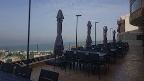 An outdoor seating area with tables and chairs, umbrellas, and a view of the cityscape. - Maximus Hotel Byblos (Blat)