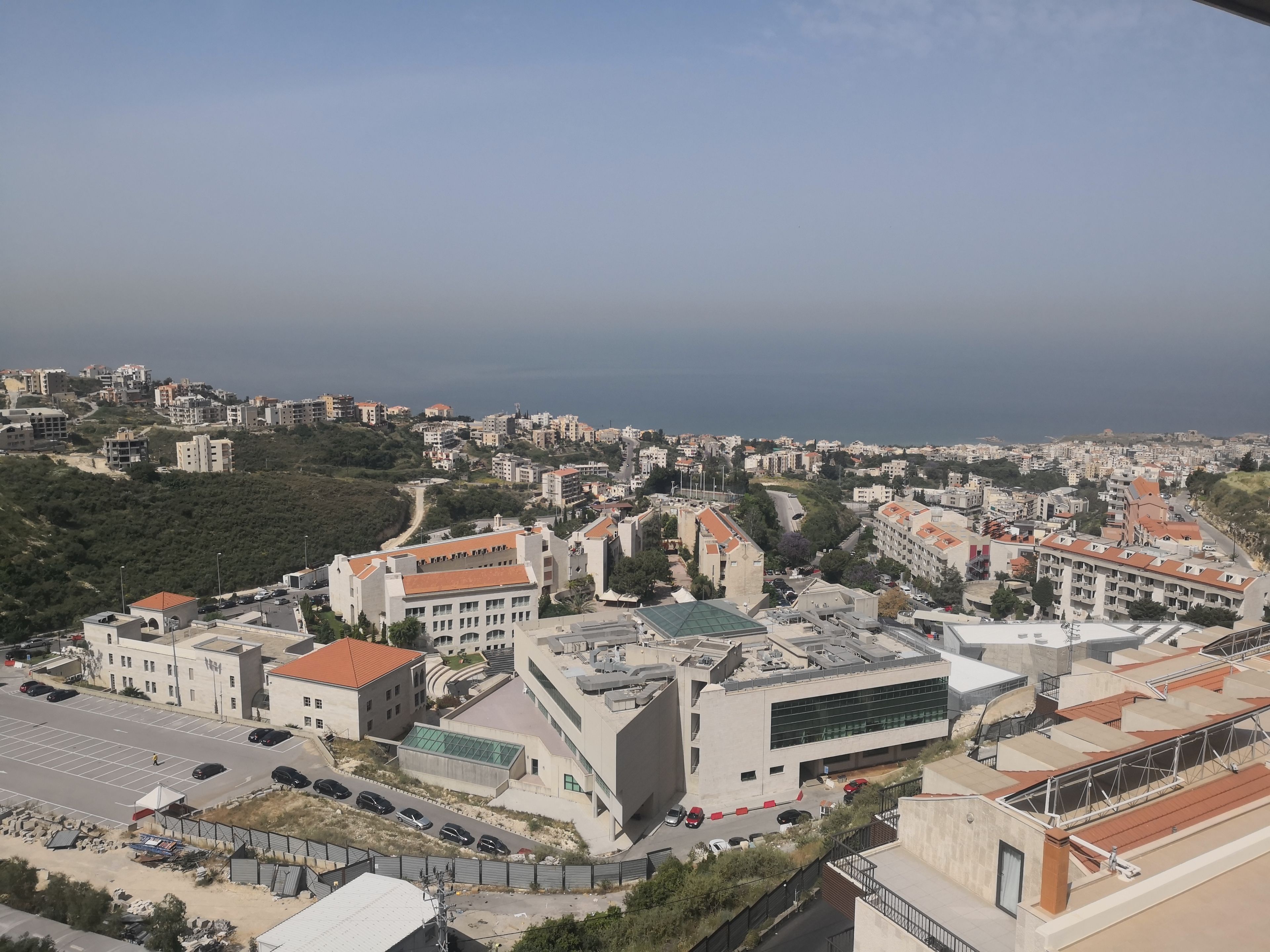 A coastal cityscape with modern buildings, a large parking area, and a view of the sea.
