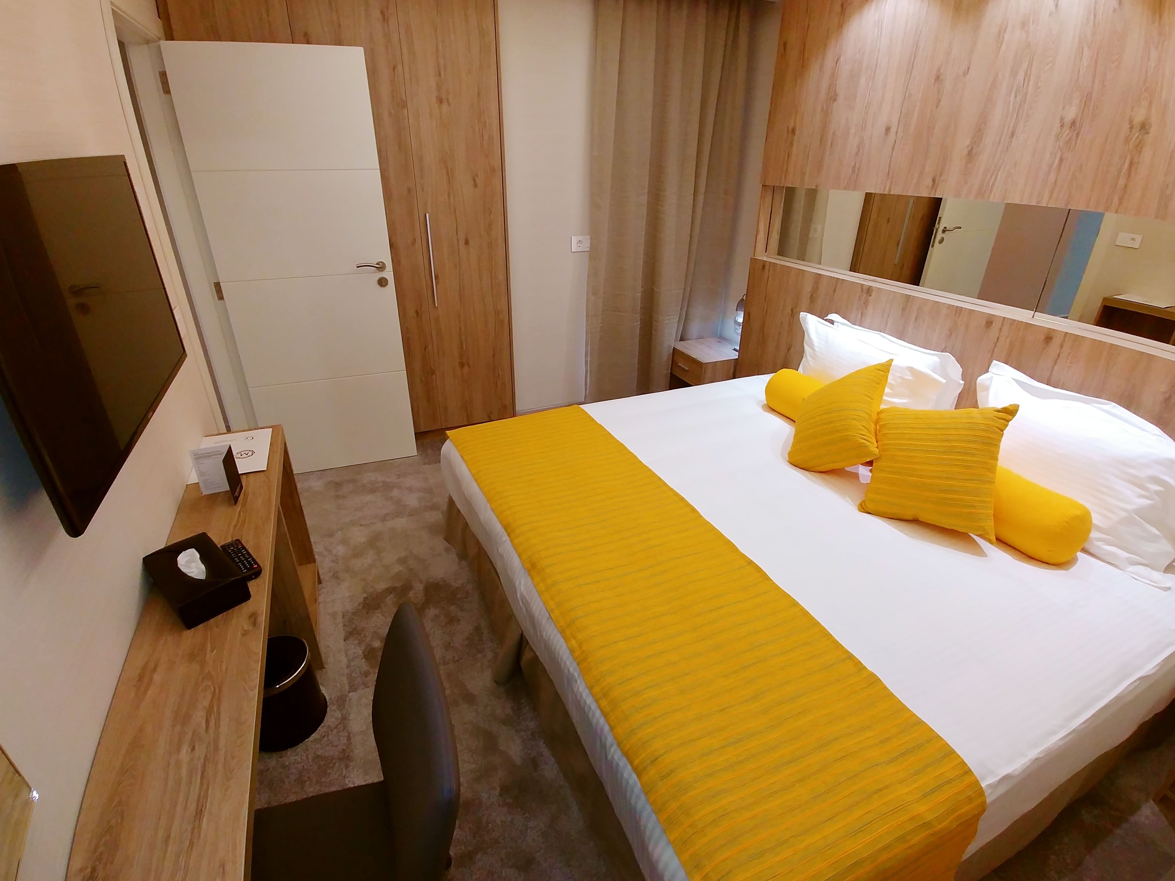 Habitación de hotel con cama, escritorio, silla, espejo y armario.