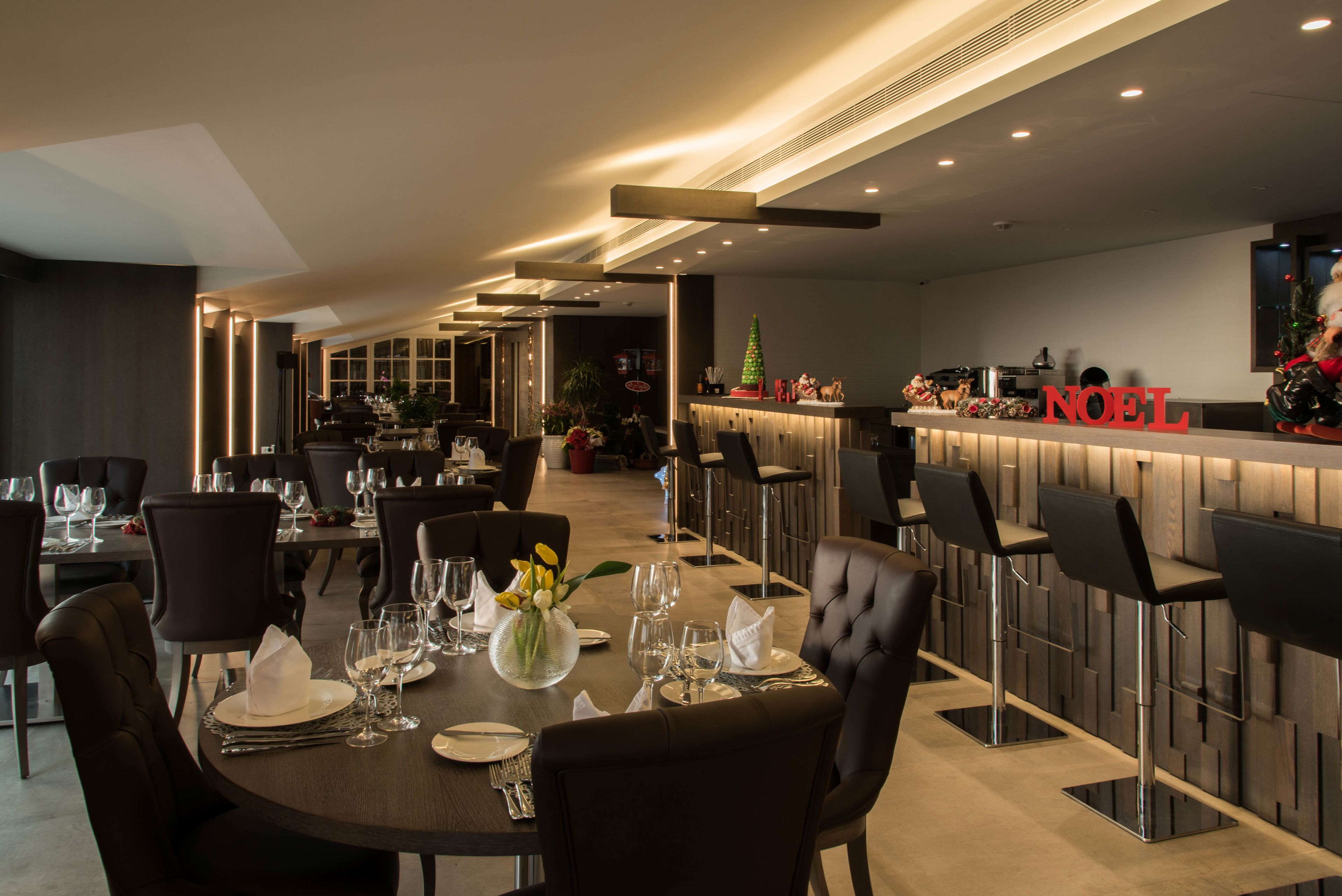 A modern dining area with a long table set for a meal, bar stools, and a Christmas tree decoration.