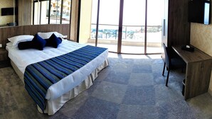 A hotel room with a large bed, a desk, a flat-screen TV, and a balcony with a city view. - Maximus Hotel Byblos (Blat)