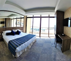 Habitación de hotel con una cama grande, un escritorio, un televisor de pantalla plana y un balcón con vistas a la ciudad.