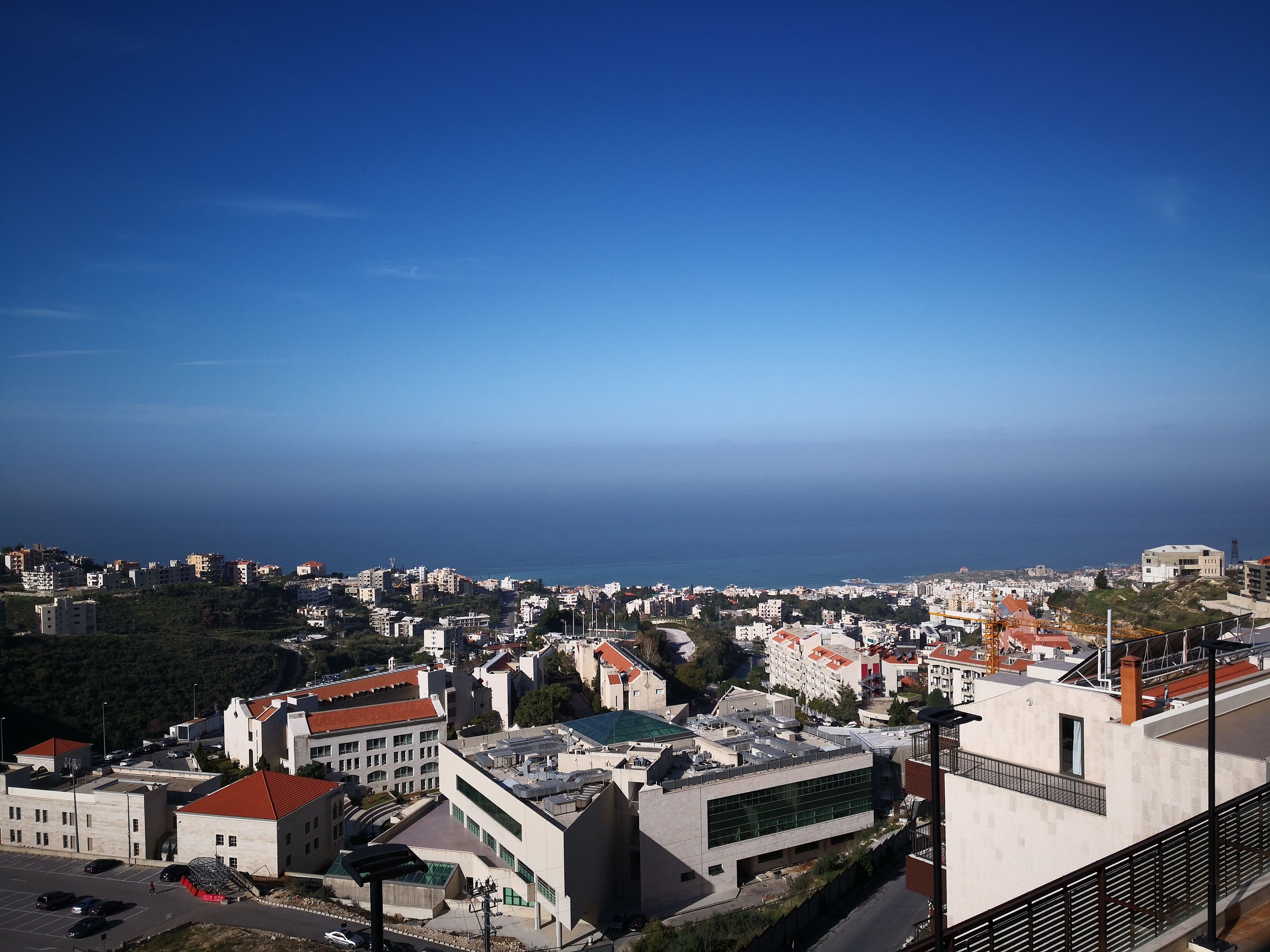 A coastal cityscape with modern buildings, a clear sky, and a view of the sea.