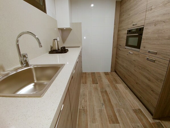 A modern kitchen with a stainless steel sink, a kettle, and wooden cabinets.