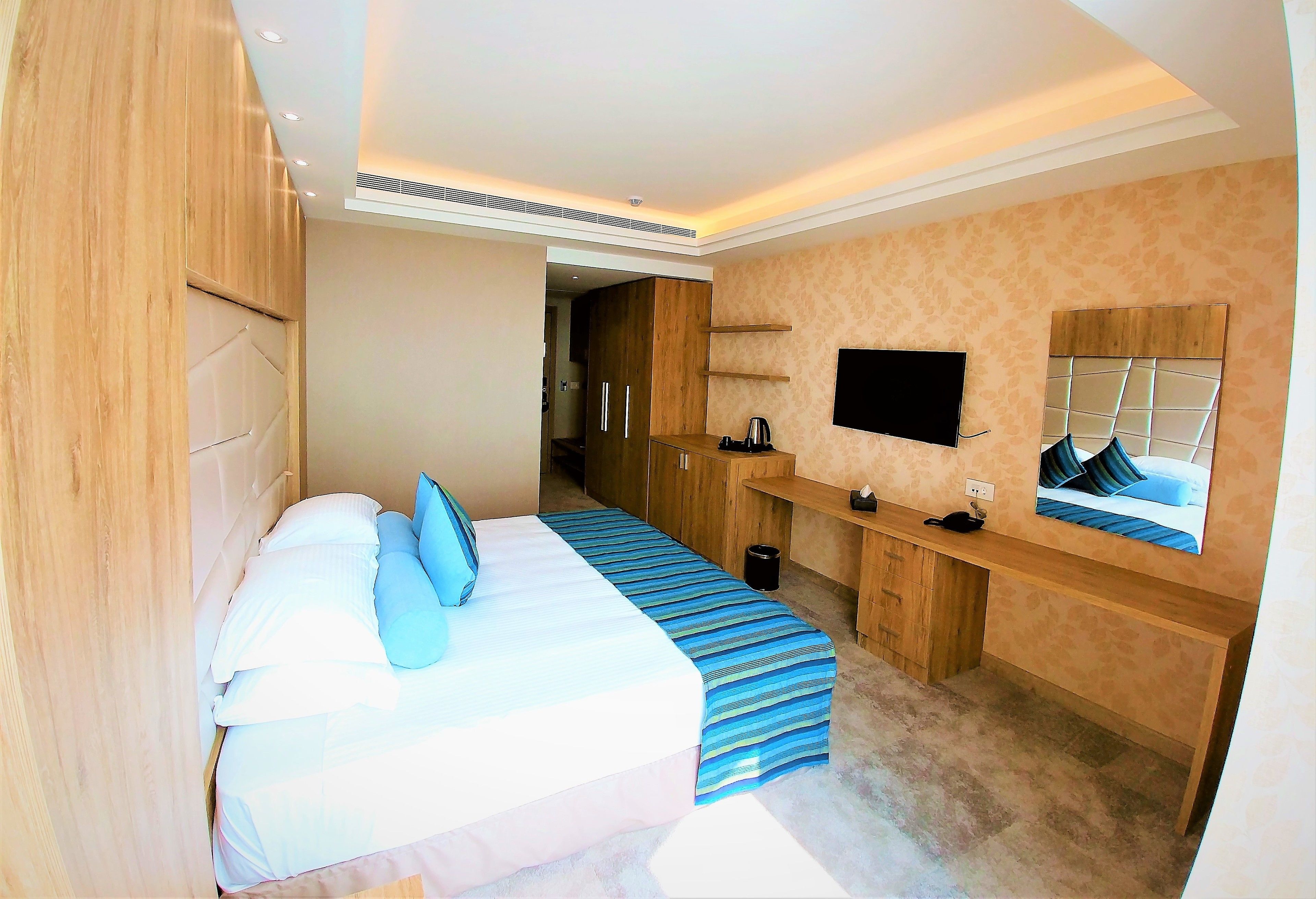 A hotel room with a bed, a desk, a chair, a television, and a mirror.