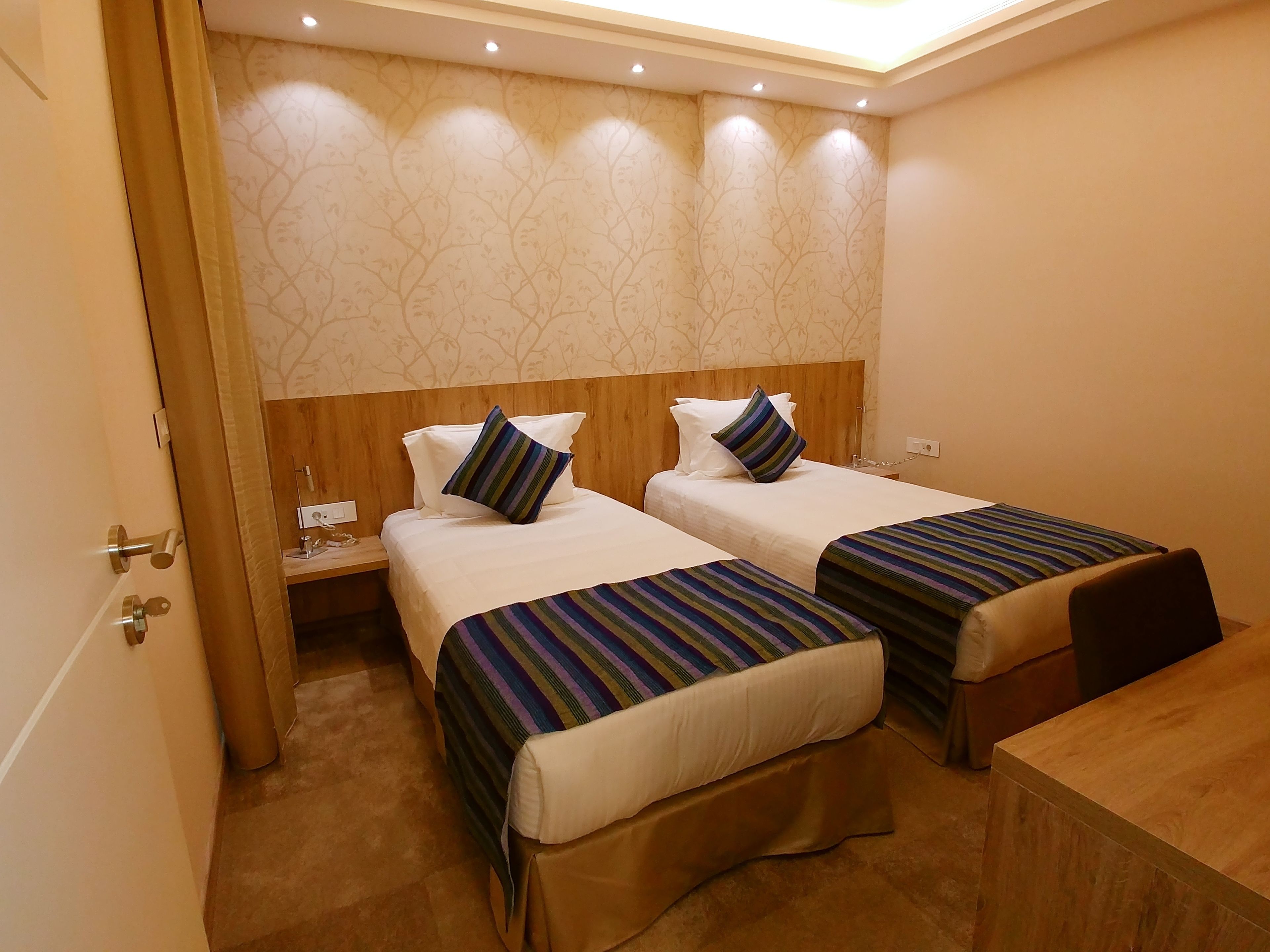 A hotel room with two beds, wooden headboards, and a nightstand with a lamp.