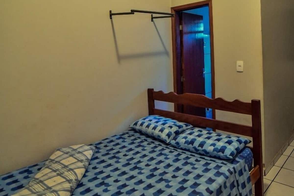 A small, single-bed room with a wooden headboard, a pull-up bar, and a door leading to another room.