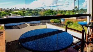 A balcony with a round table and chairs, large windows offering a view of a cityscape and greenery. - Hotel Califórnia (Jatai)