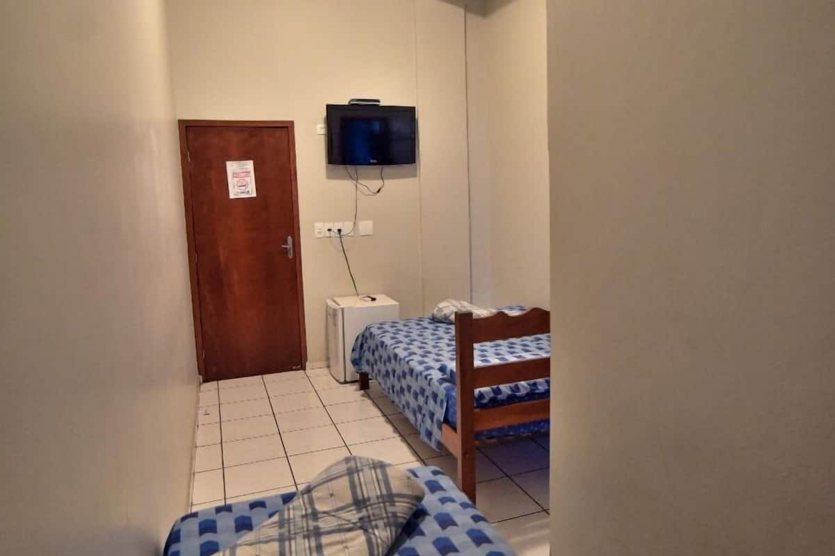 A narrow hallway with a bed, a television mounted on the wall, and a door at the end.
