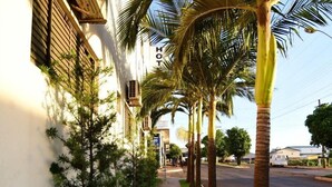 A sidewalk lined with palm trees and a building with air conditioning units. - Hotel Califórnia (Jatai)