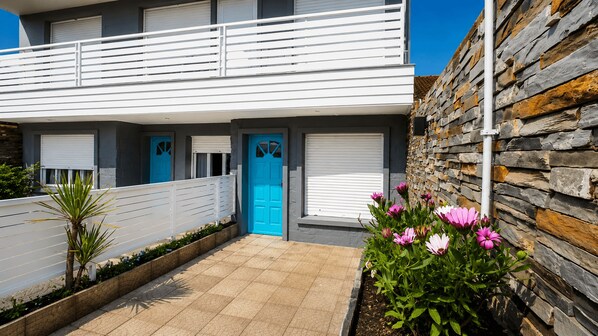 A modern two-story house with a balcony, a blue door, and a stone wall.