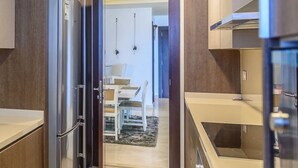 A compact kitchen with a built-in refrigerator, a dining area with a table and chairs, and a microwave. - Amara Suites - Eko Atlantic (Lagos)