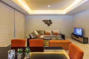 A modern living room with a sofa, coffee table, and TV. - Amara Suites - Eko Atlantic (Lagos)