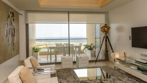 A modern living room with a large sliding glass door leading to a balcony with a view of the beach. - Amara Suites - Eko Atlantic (Lagos)