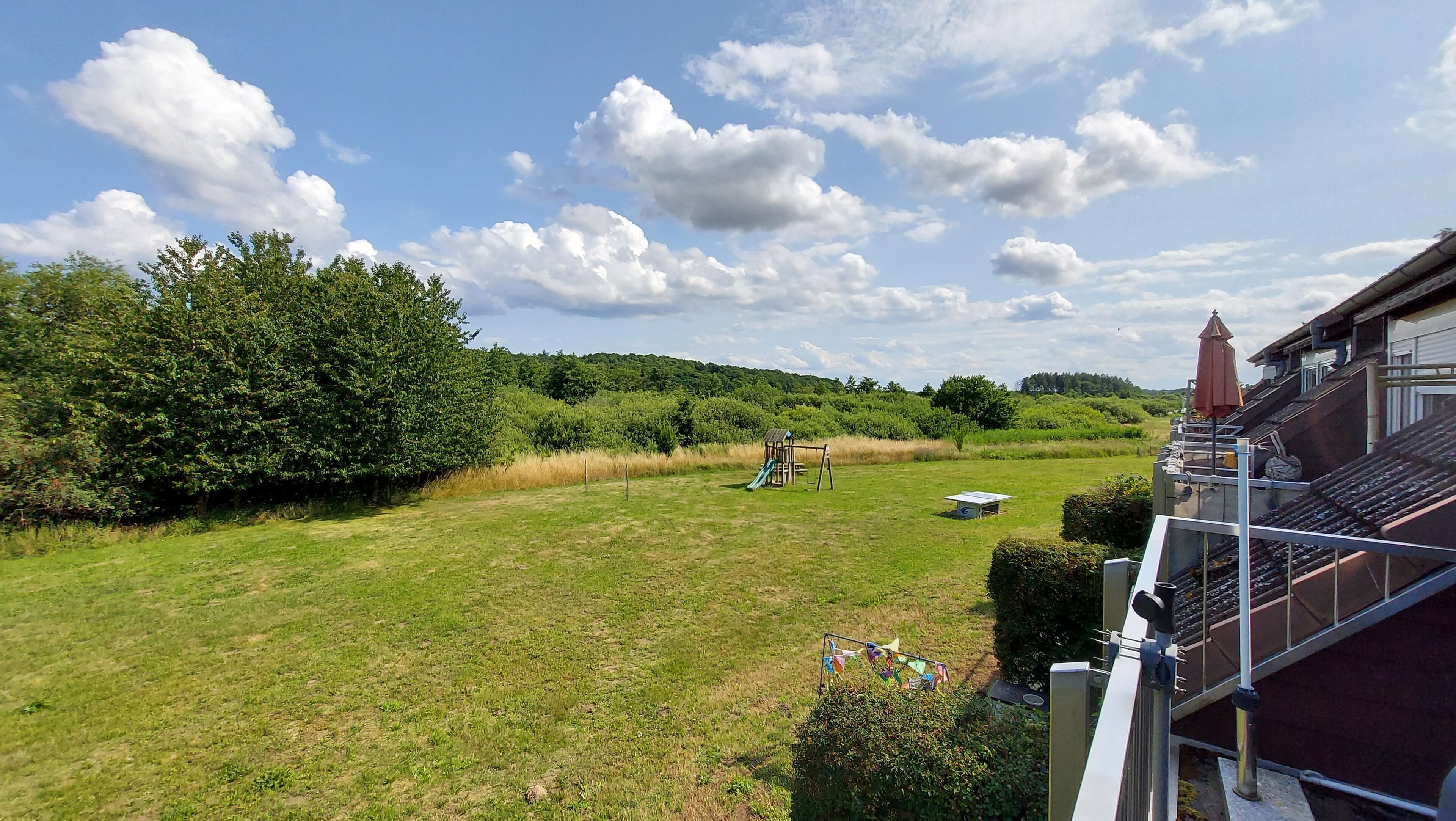 A grassy field with a playground, a building with a red roof, and a clear sky with clouds.