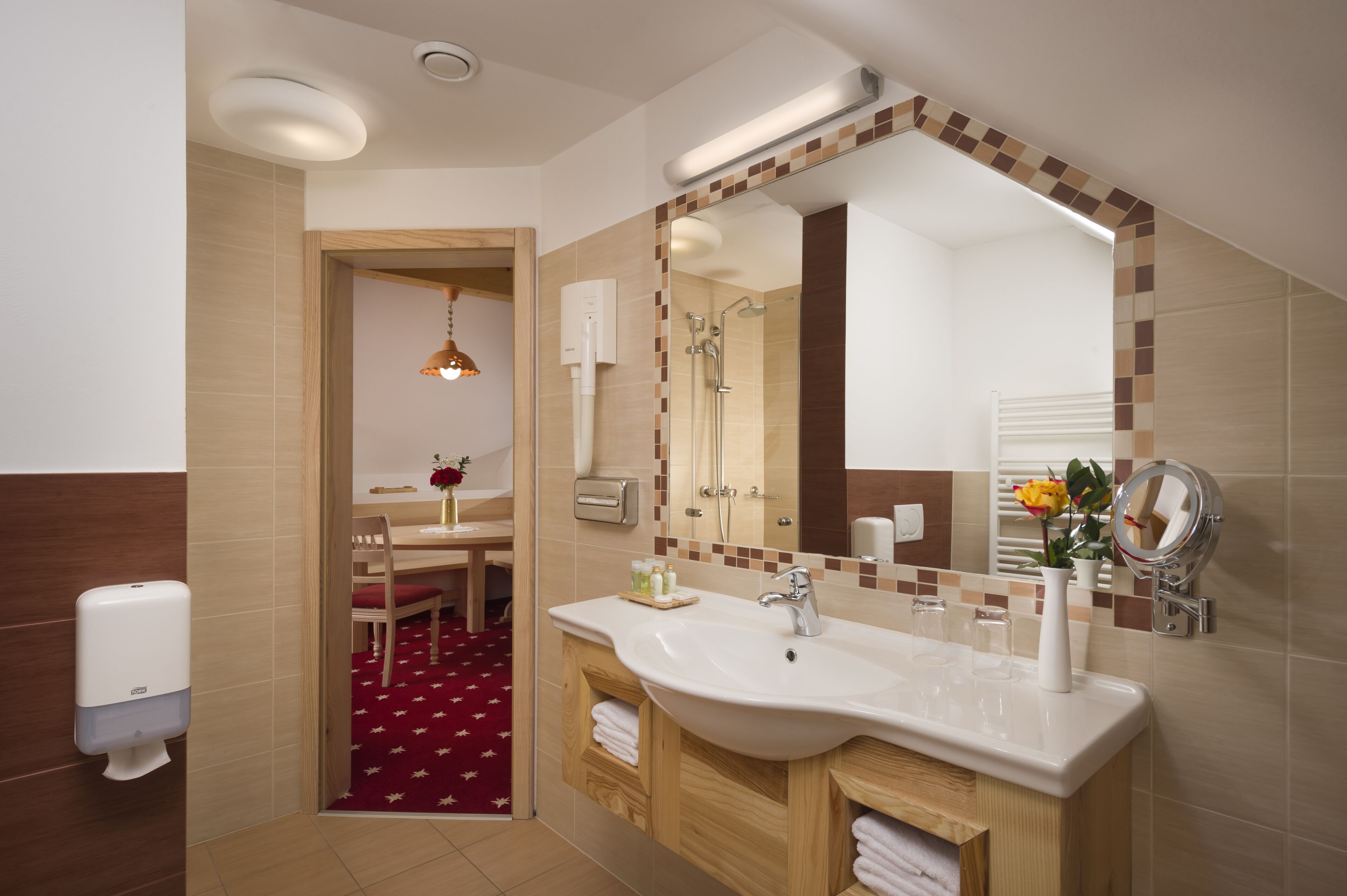 A modern bathroom with a large mirror, a sink, and a shower. There is a wooden vanity and a red carpeted area.