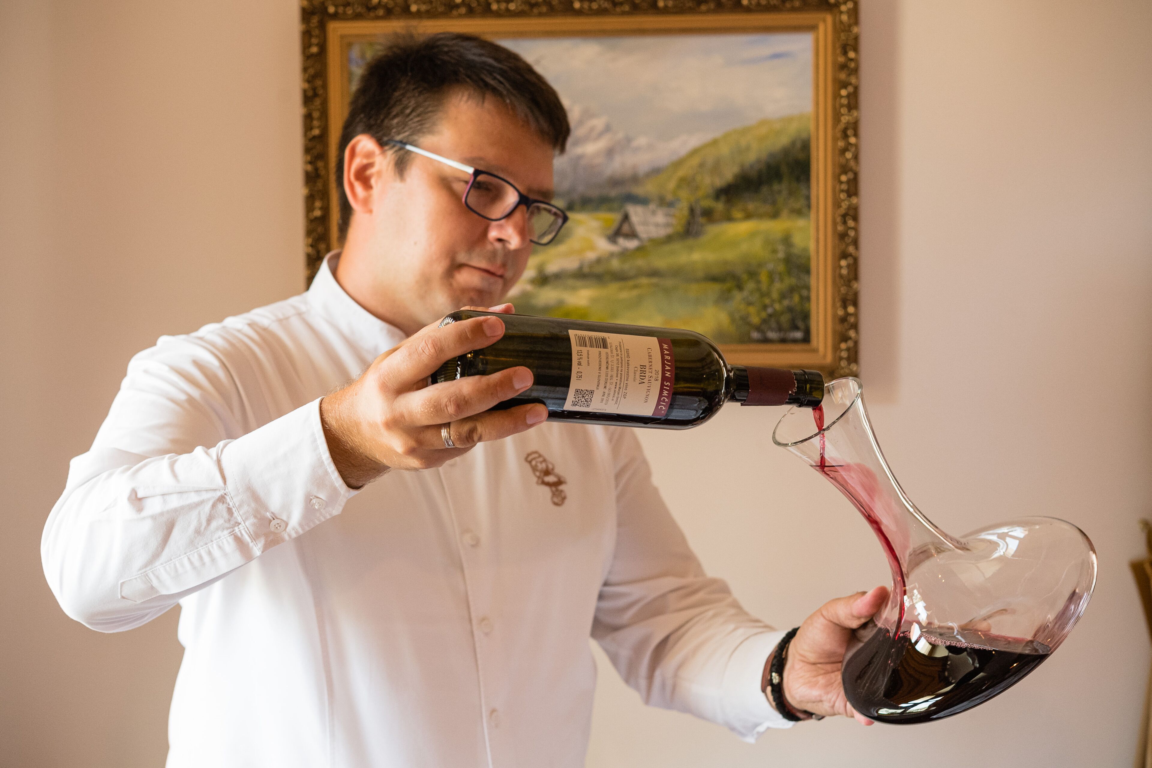A person pouring red wine from a bottle into a glass.