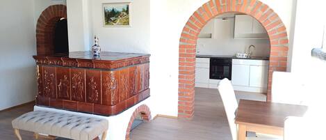 A room with a wooden cabinet, a cushioned bench, a dining table, and a kitchen area with a brick archway.