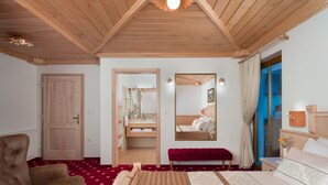 A bedroom with a wooden ceiling, a large bed, a bench, a mirror, and a view of the outside. - Hotel Planinka (Ljubno)