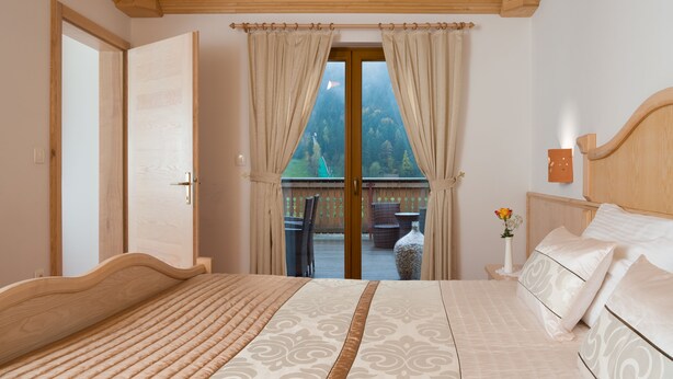 A bedroom with a large bed, wooden headboard, and a view of a balcony with outdoor furniture. - Hotel Planinka (Ljubno)