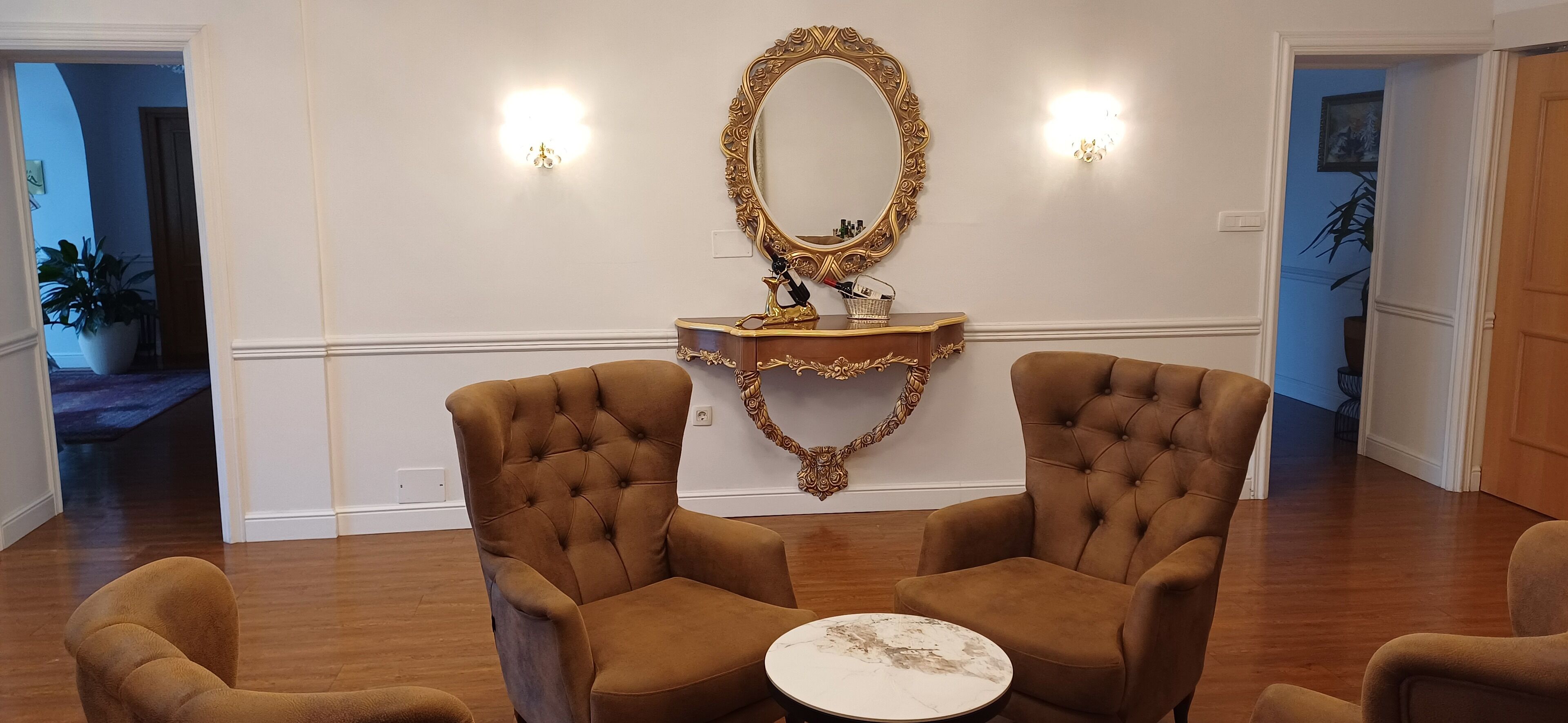 Een kamer met twee bruine fauteuils, een ronde witte tafel en een spiegel met gouden lijst.