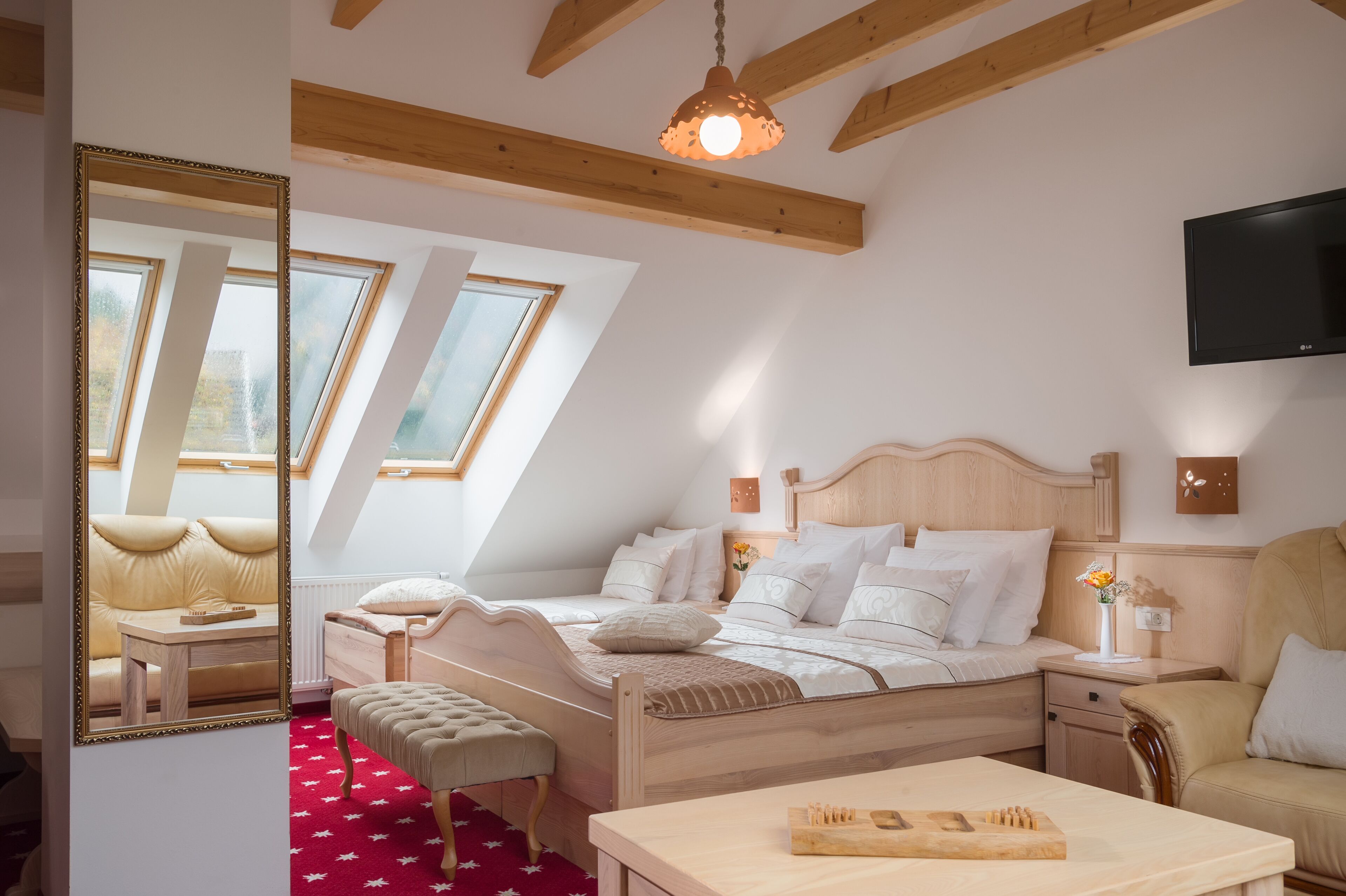 Une chambre à coucher avec un lit en bois, une table de chevet, une chaise, un miroir et un téléviseur fixé au mur.