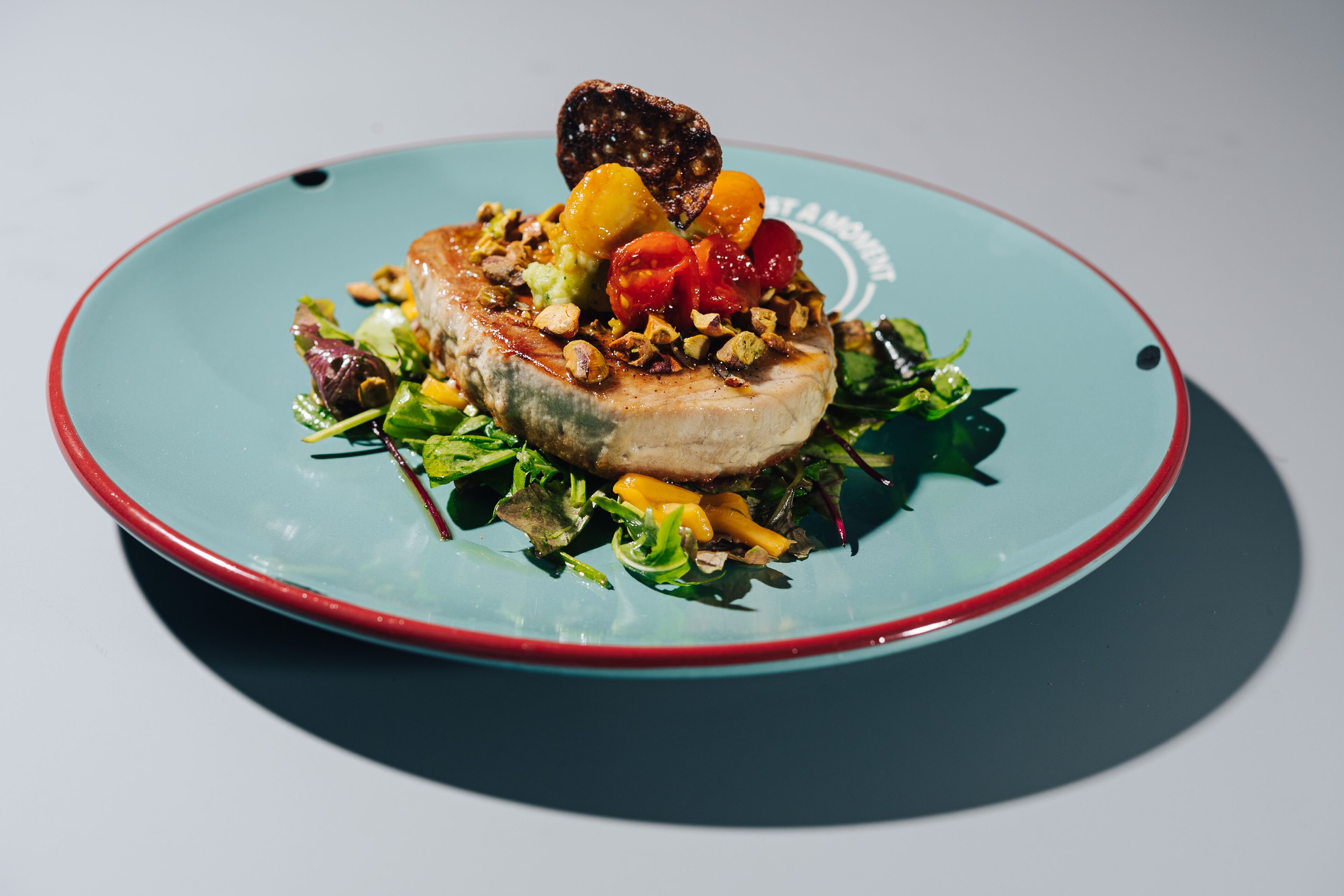 Een bord eten met vlees, groenten en garnering op een blauw bord.
