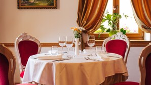 A dining table set with white tablecloth, red upholstered chairs, and a vase with flowers. - Hotel Planinka (Ljubno)