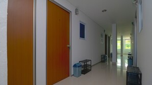 A hallway with wooden doors, a trash bin, and a small shelf. - RedDoorz Plus Near Kepri Mall (Batam)
