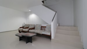 A modern living room with a sofa, coffee table, and a staircase. - RedDoorz Plus Near Kepri Mall (Batam)