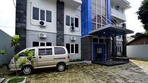 A modern building with a beige van parked in front, air conditioning units, and a blue entrance. - RedDoorz near Museum Keraton Surakarta (Surakarta)