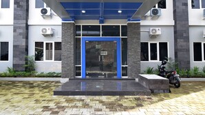 A building entrance with a blue and white facade, air conditioning units, and a motorcycle parked outside. - RedDoorz near Museum Keraton Surakarta (Surakarta)