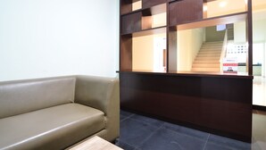 A reception area with a brown leather sofa, a dark wooden reception desk, and a tiled floor. - RedDoorz near Museum Keraton Surakarta (Surakarta)