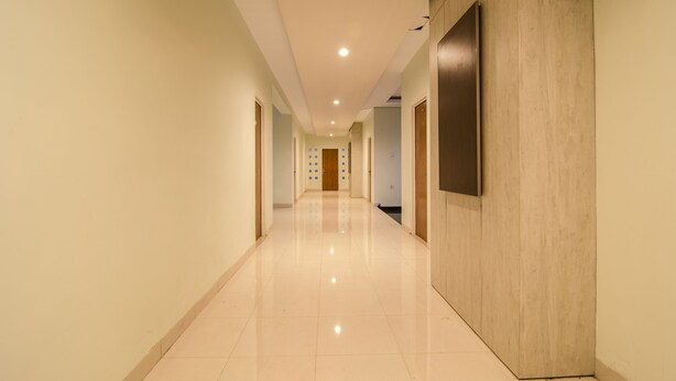 A long, well-lit hallway with a tiled floor, wooden paneling on one side, and doors leading to rooms. - RedDoorz near Museum Keraton Surakarta (Surakarta)