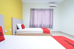 A bedroom with a bed, a yellow wall, a grey curtain, and an air conditioning unit. - RedDoorz near Museum Keraton Surakarta (Surakarta)