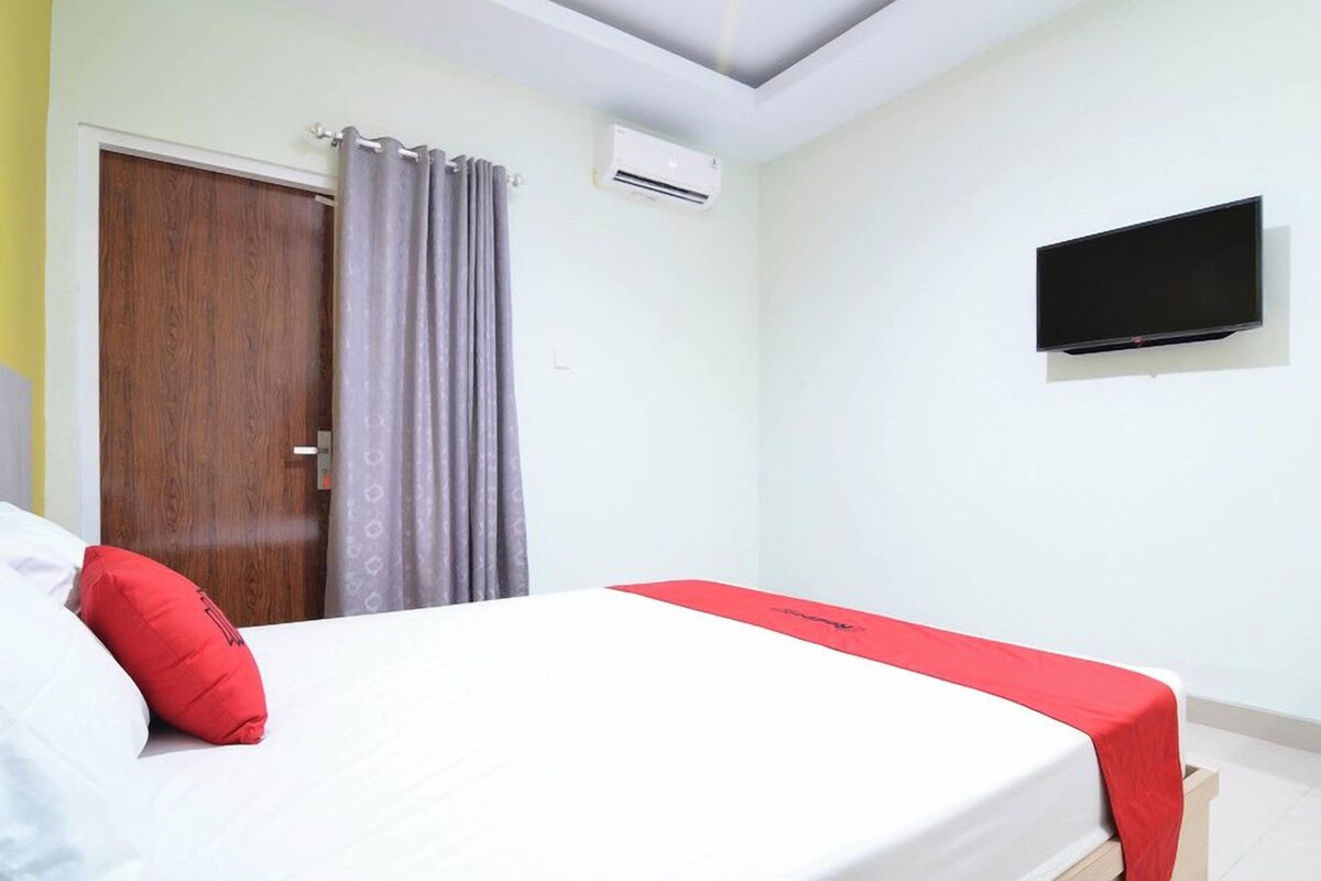 A hotel room with a bed, a television, an air conditioning unit, and a wooden door.