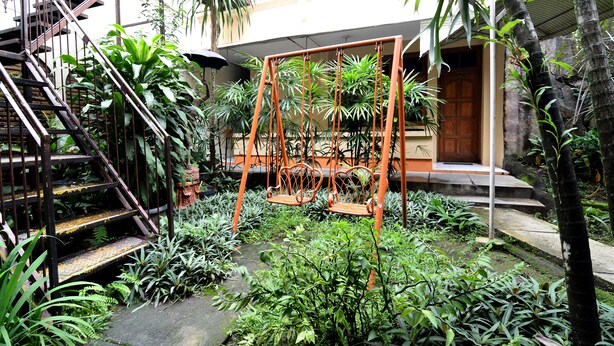 A courtyard with a staircase, swing set, and lush greenery. - RedDoorz Plus @ Laweyan (Surakarta)