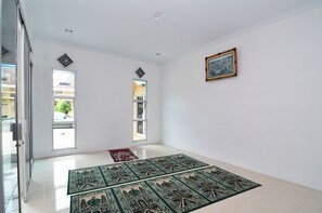 Een ruime kamer met grote ramen, een rood vloerkleed en een ingelijst schilderij aan de muur.