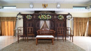 A room with a wooden sofa set, two chairs, a small table, and a decorative wall with floral arrangements. - RedDoorz Plus @ Laweyan (Surakarta)