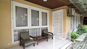 A balcony with two chairs and a table, a white door, and an air conditioning unit. - RedDoorz Plus @ Laweyan (Surakarta)