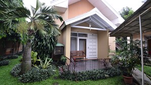 A residential building with a covered porch, a bench, and a variety of tropical plants. - RedDoorz Plus @ Laweyan (Surakarta)